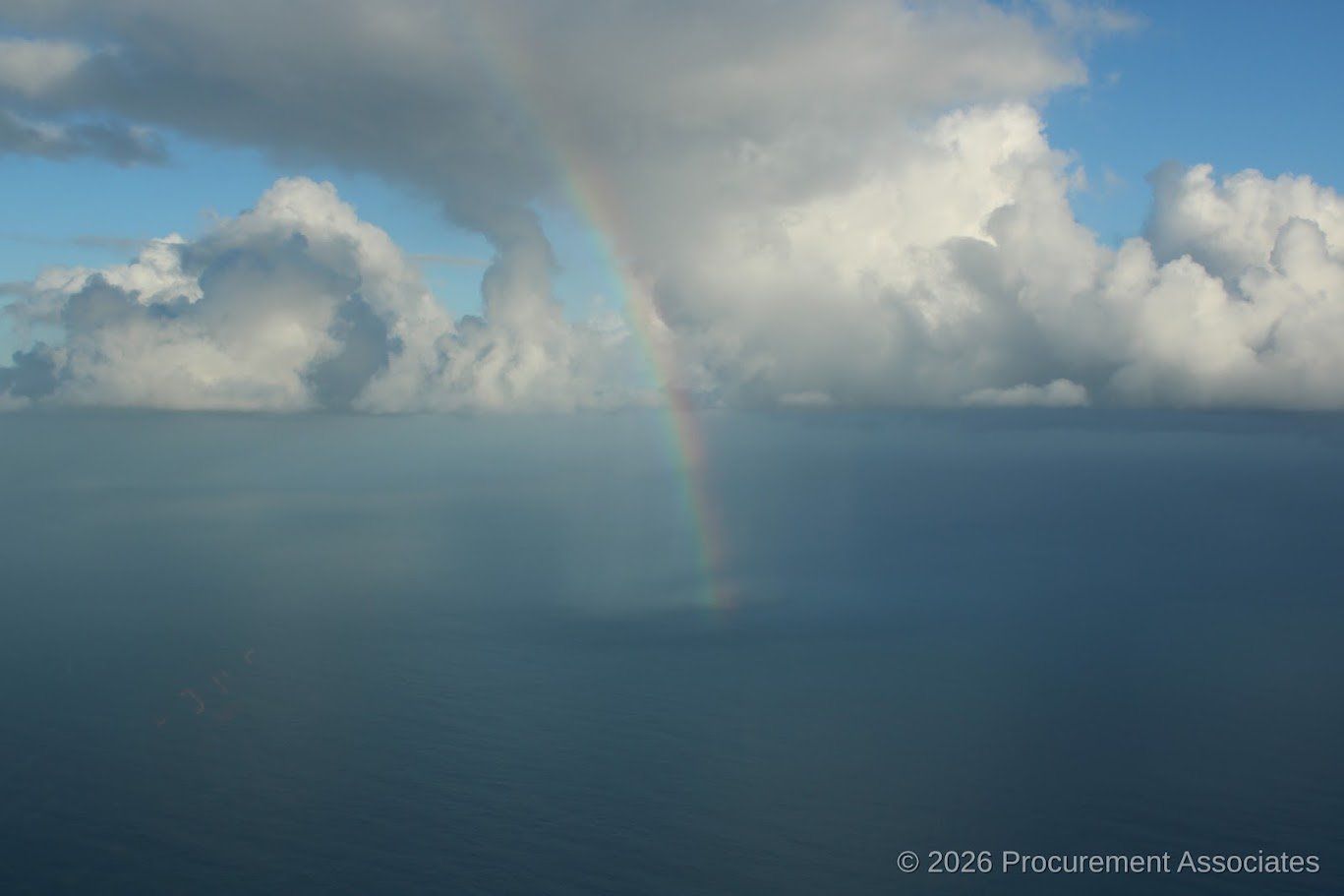 A rainbow over the ocean with clouds in the sky.