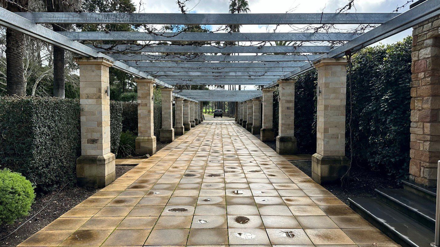 Covered stone walkway with columns and a garden setting.