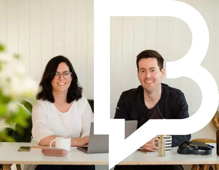 Two people sitting at a desk with laptops.