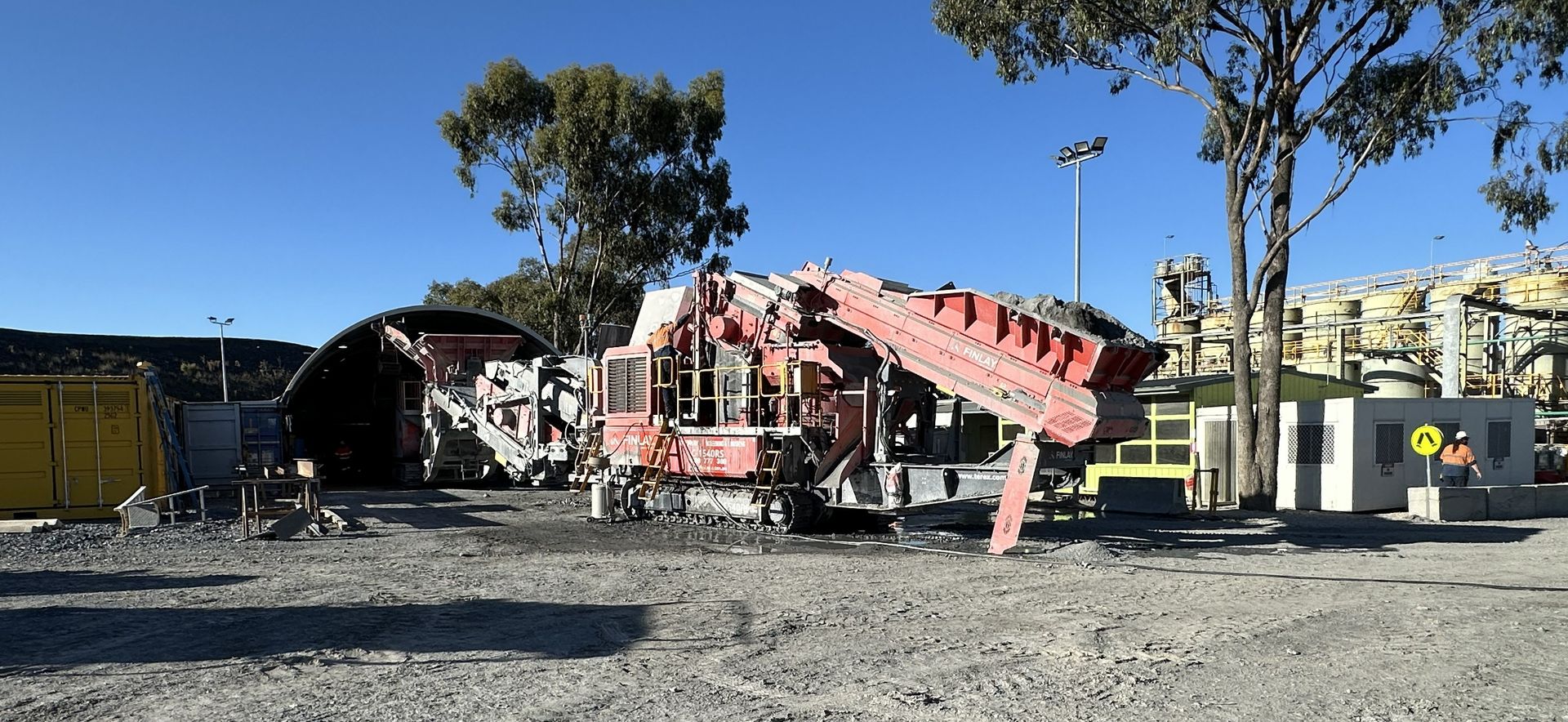 Industrial machinery at a construction site with trees and buildings in the background.