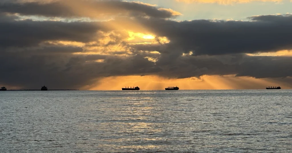 Ships silhouetted against dramatic sunset over ocean.