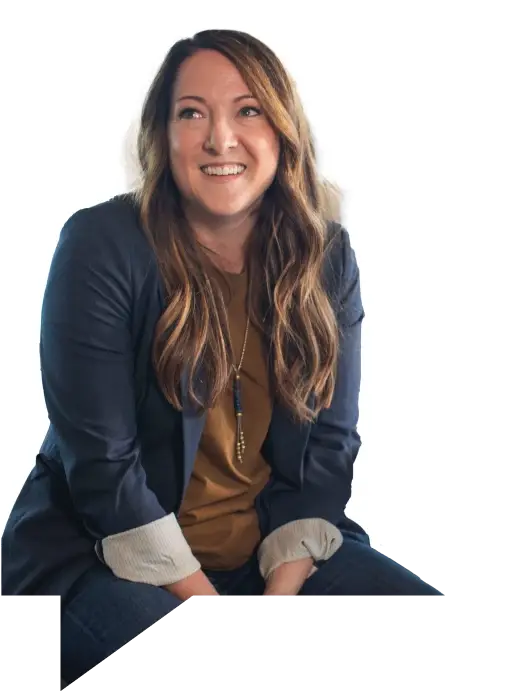 Smiling woman seated casually in a blazer and jeans.