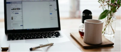 Laptop, coffee mug, and notebook on a tidy desk setup by a window.