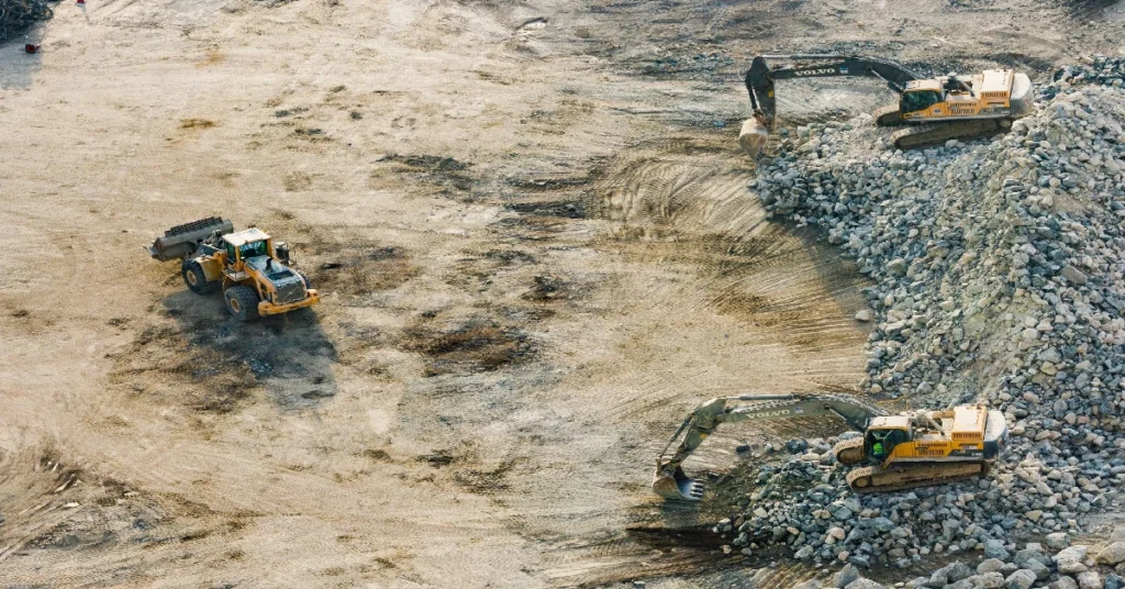 Excavators and loader moving gravel at construction site.