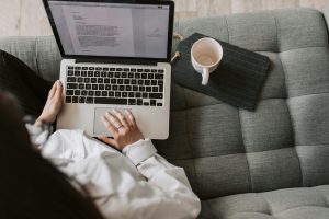 Person typing on a laptop while seated on a couch with coffee nearby — featured image for article on writing tenders for beginners.