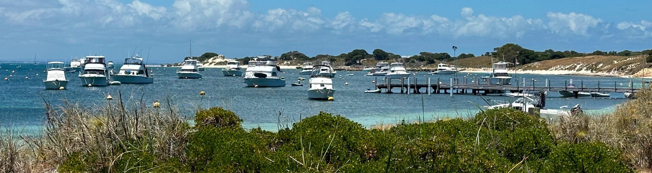 Boats anchored near a wooden jetty in clear water.